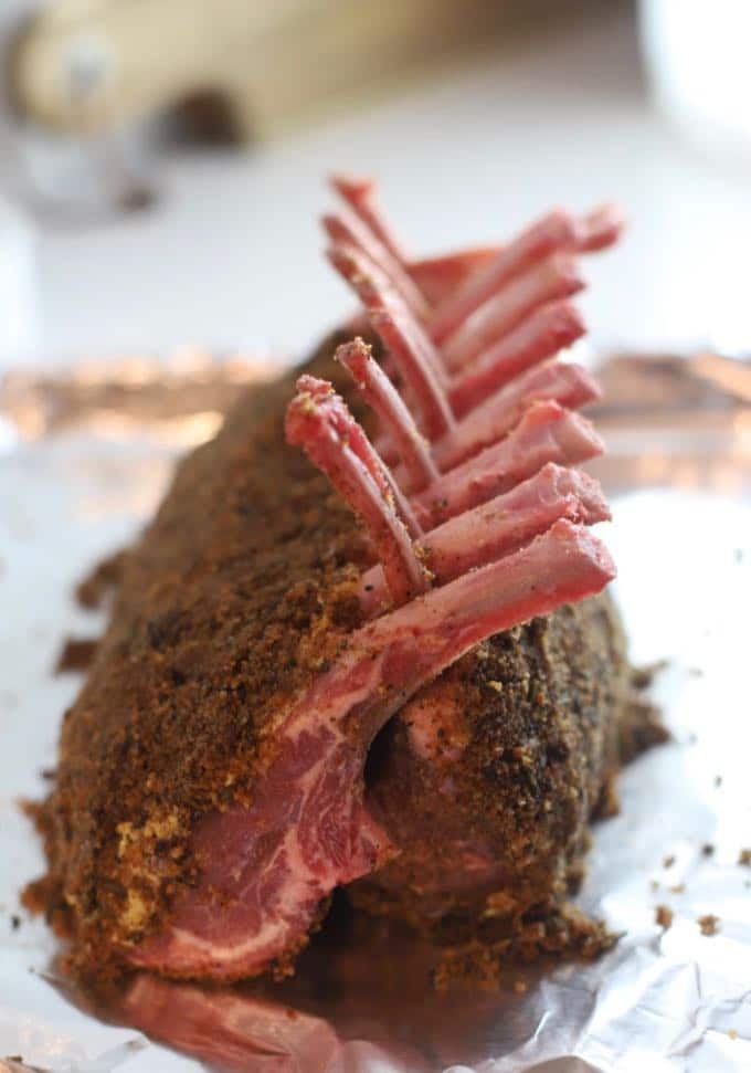 Two racks of lamb covered with a herb and breadcrumb topping on a baking sheet ready for the oven.