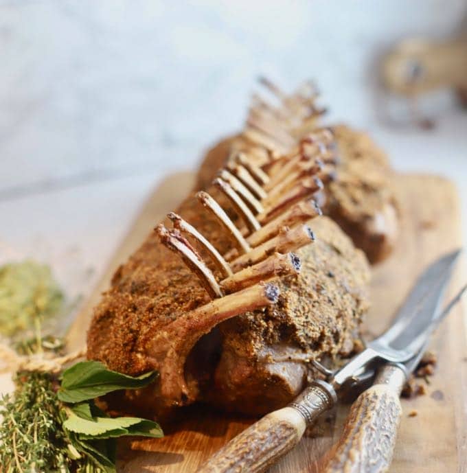 Roasted Rack of Lamb on a wooden cutting board with a serving knife and fork. 