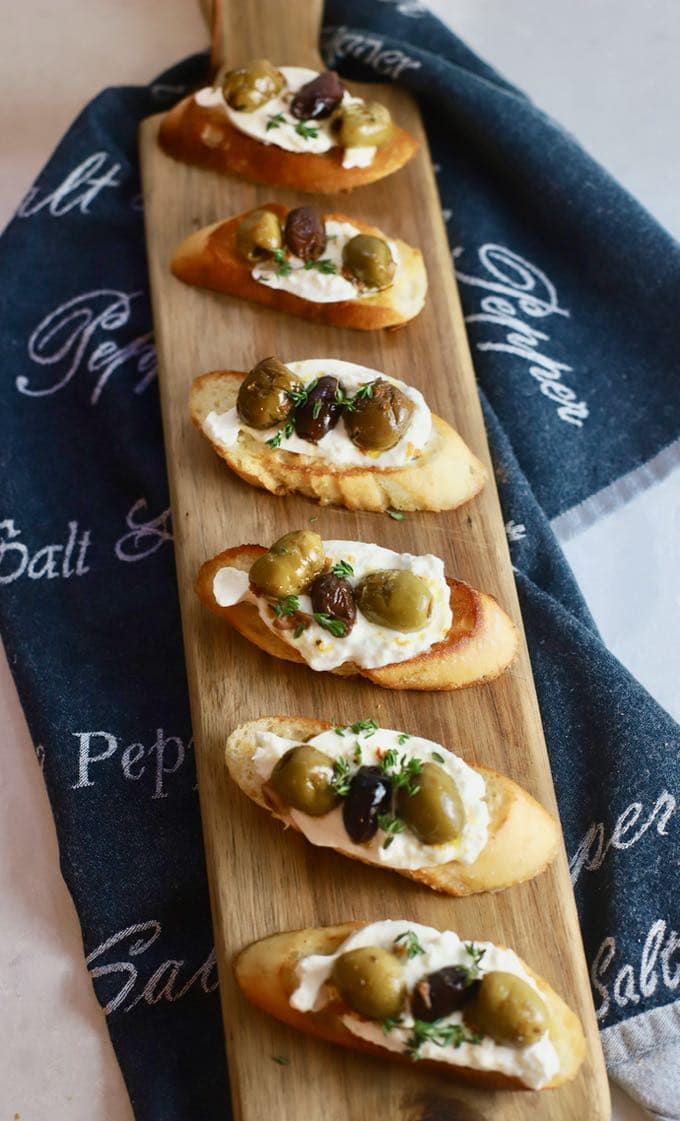 Six slices of bruschetta on a wooden board with a gray napkin underneath.