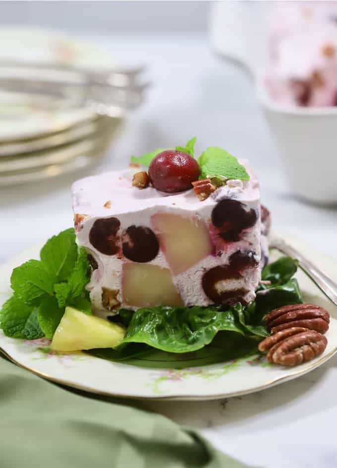 A serving of frozen fruit salad on a plate garnished with cherries and a piece of pineapple. 