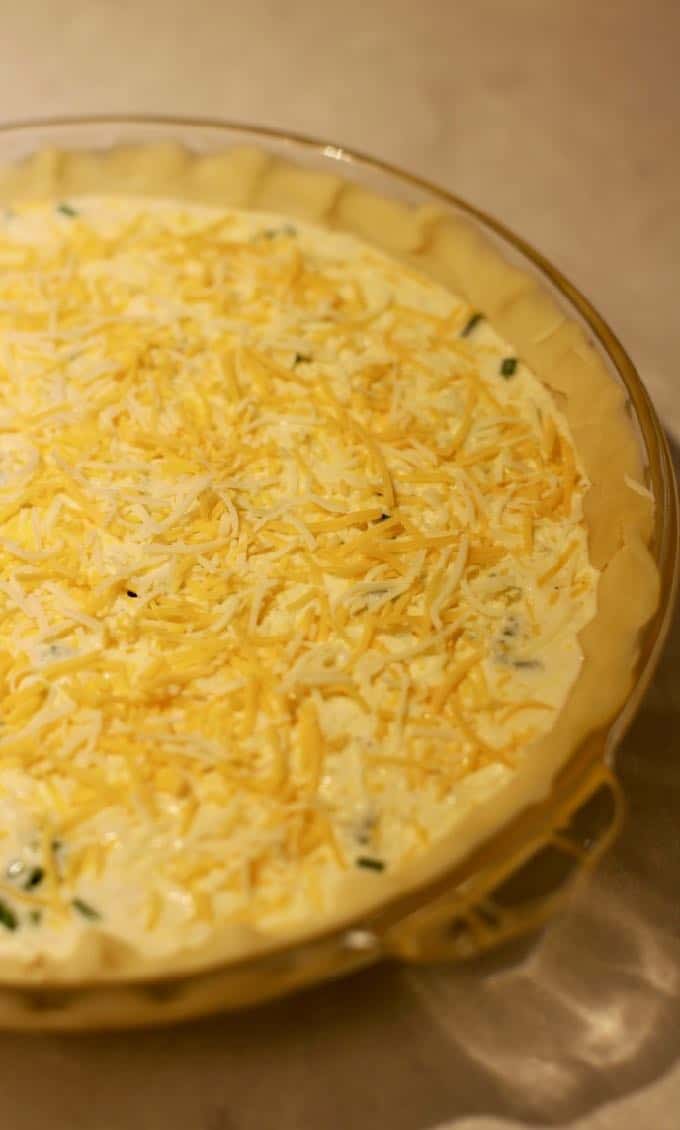 An unbaked ham and cheese quiche in a glass baking dish ready for the oven.