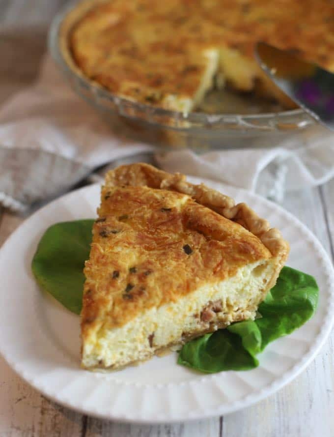A slice of ham and cheese quiche on a white plate. 