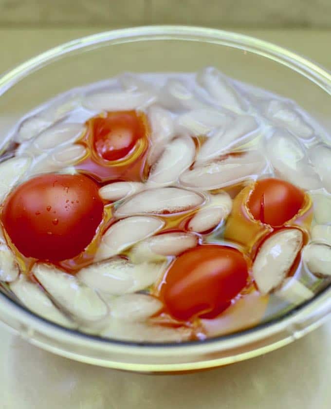 Tomatoes in a clear glass bowl with ice and water.