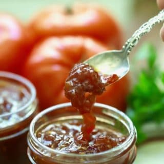 A spoonful of tomato jam being taken out of a jar.