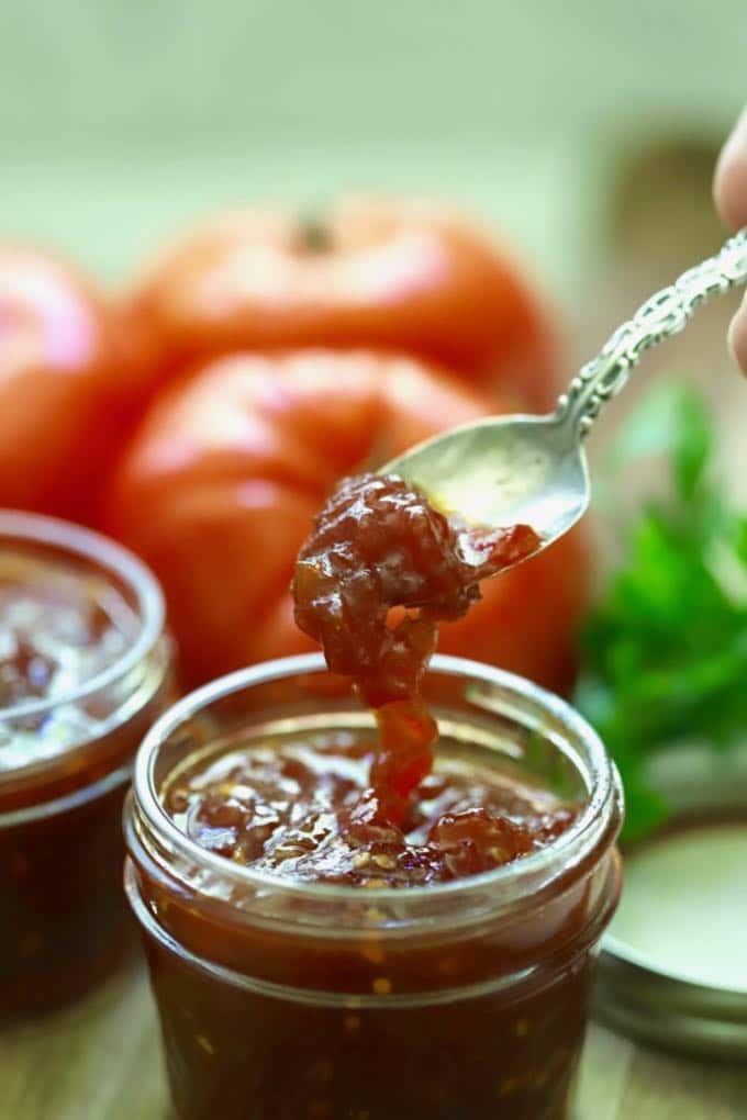 A spoonful of tomato jam being taken out of a jar.