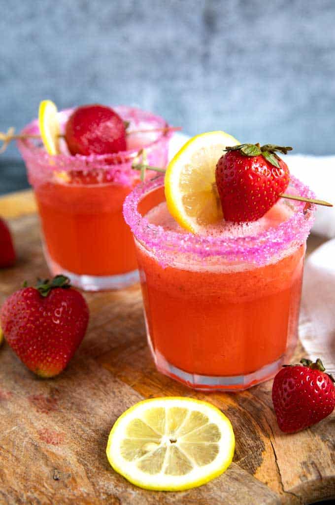 Two glasses of Strawberry Lemonade Vodka topped with lemon slices and strawberries.