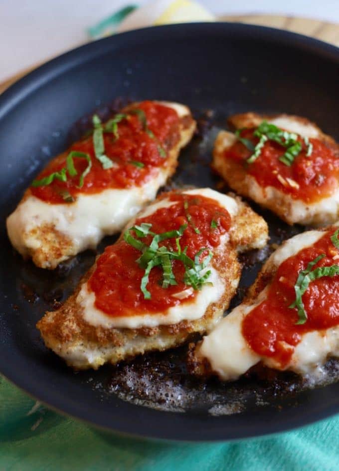 Four chicken breasts in a skillet topped with tomato sauce, mozzarella cheese and chopped basil. 