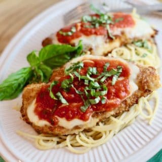 Chicken Parmesan served over spaghetti on a white plate.