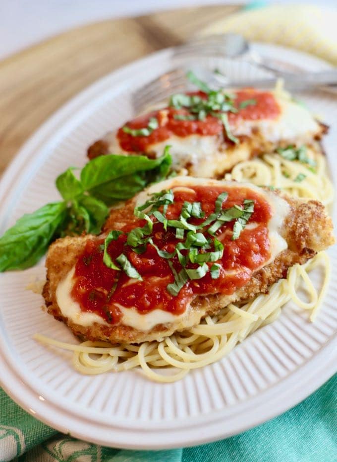 Chicken Parmesan served over spaghetti on a white plate.