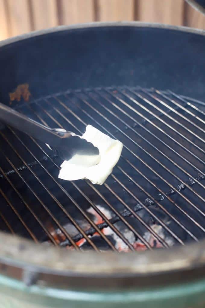 Using tongs with a folded up paper towel soaked in oil, to grease grates on an outdoor grill.