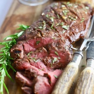 Sliced London Broil on a cutting board with a knife and fork.