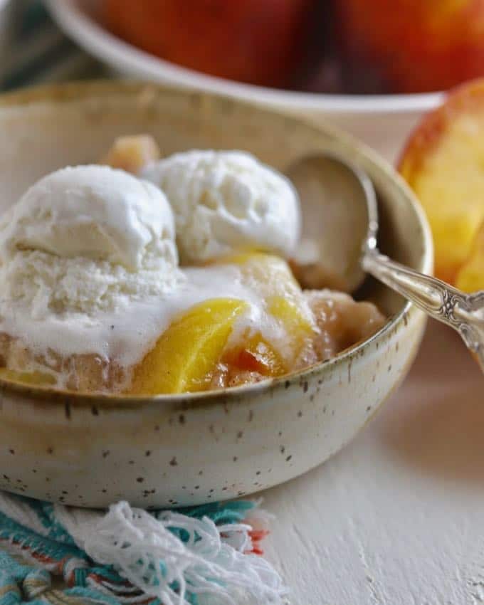 Two scoops of vanilla ice cream over peaches in a bowl.