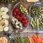 Seven glass relish trays with an assortment of marinated and pickled vegetables.