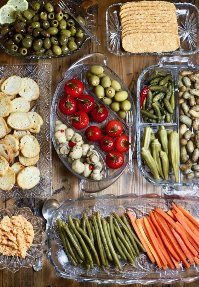 Seven glass relish trays with an assortment of marinated and pickled vegetables.