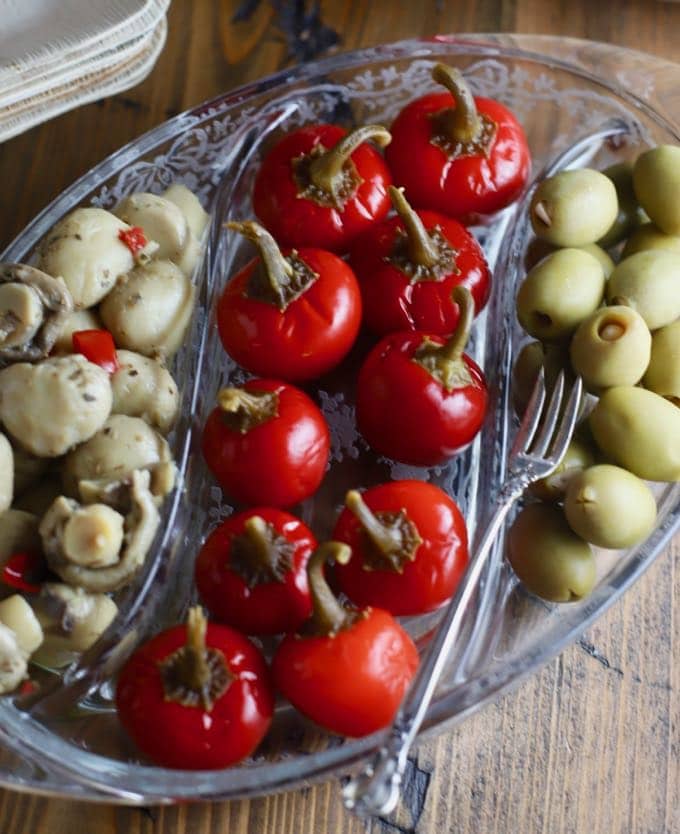 A glass dish with mushrooms, spicy cherry peppers and stuffed olives.