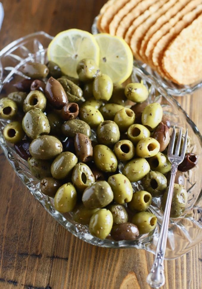 Mixed green and black olives on a glass dish garnished with lemon slices.