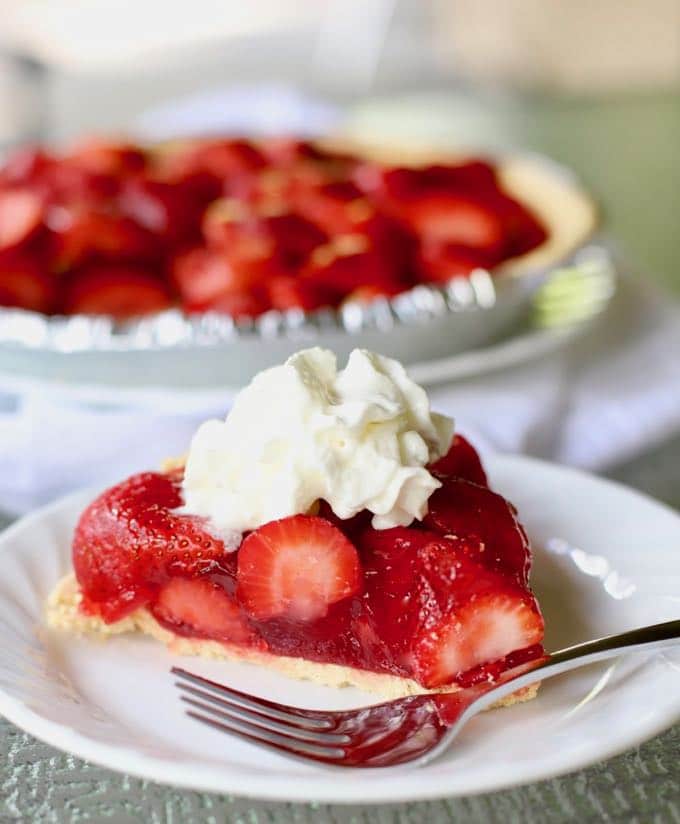 A slice of strawberry pie topped with whipped cream on a plate with a fork.