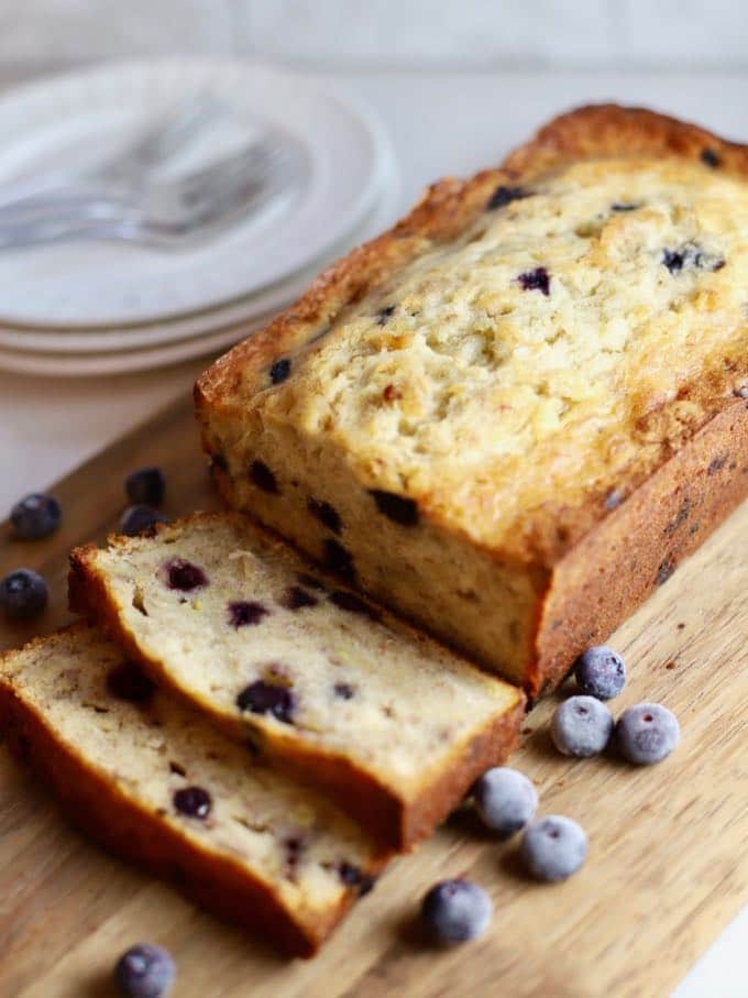 A loaf of banana bread with blueberries on a cutting board with two slices cut.
