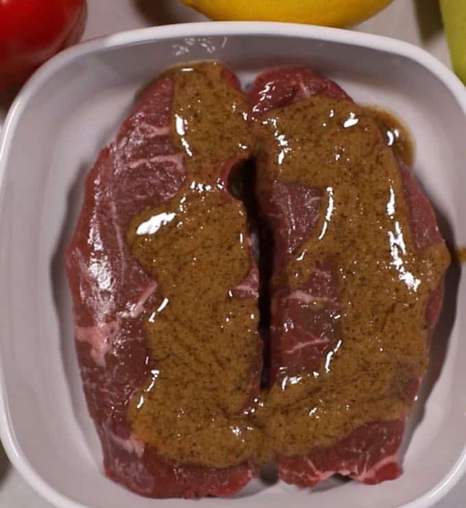 Two sirloin steaks marinating in a white dish.