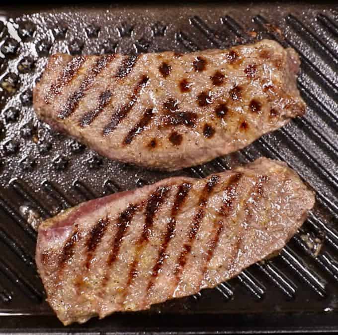 Two sirloin steaks cooking on a grill pan.