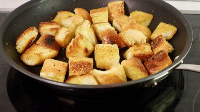 Large cubes of bread toasting in a saute pan.