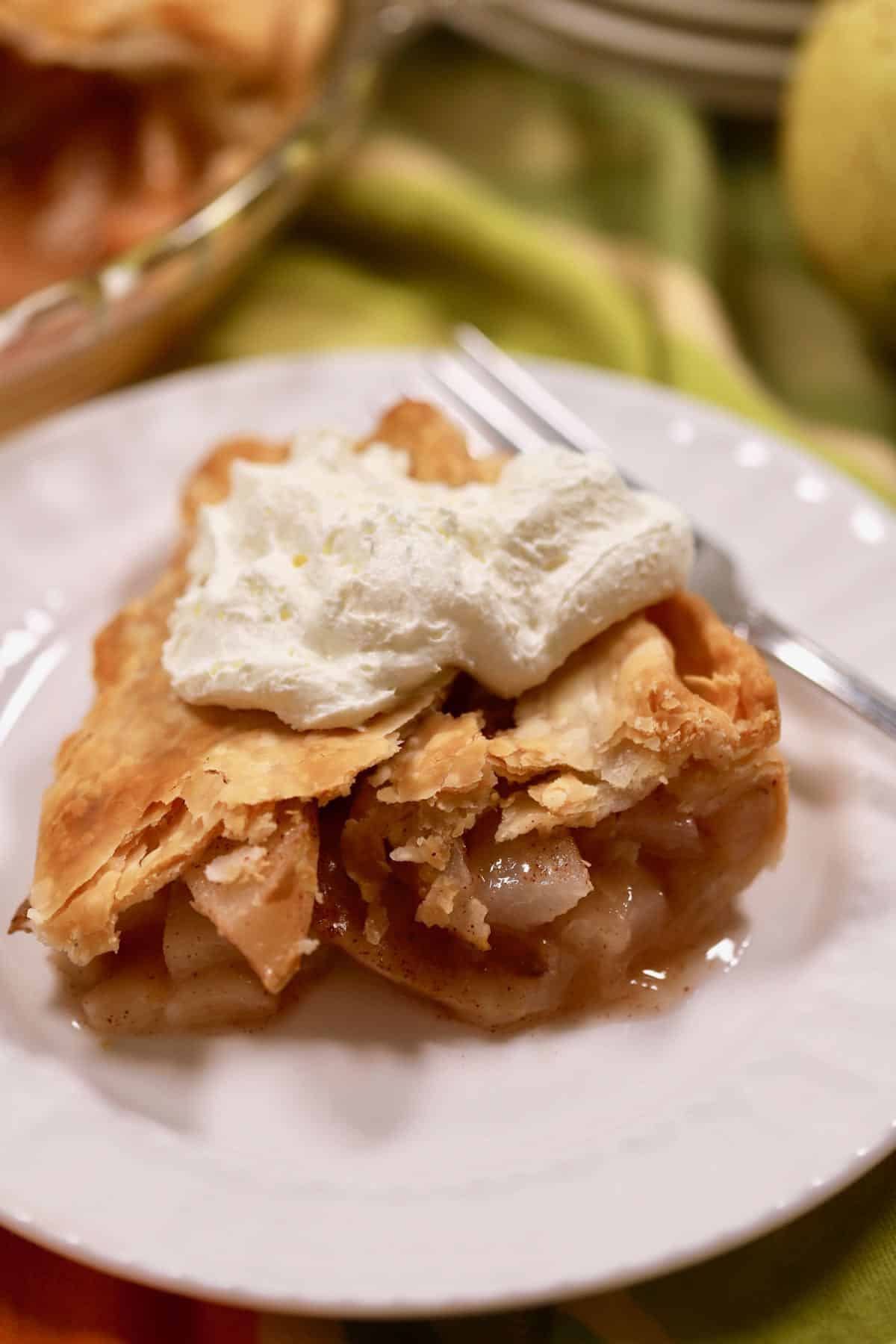 A piece of pear pie topped with whipped cream on a white plate.