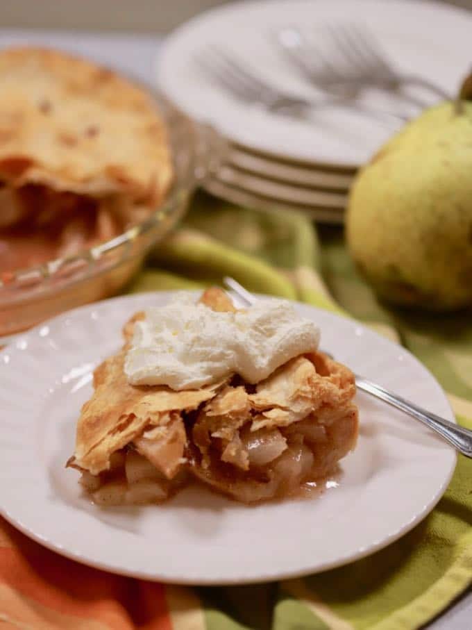 A piece of pear pie topped with whipped cream on a white plate.