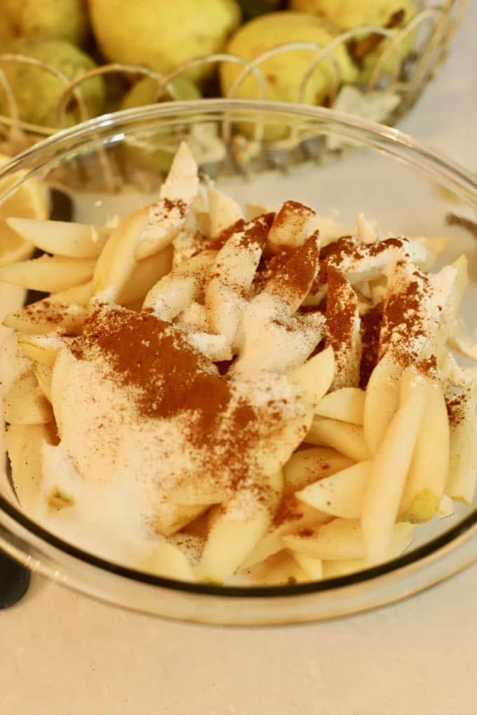 Pear slices in a glass bowl topped with sugar, flour and cinnamon.