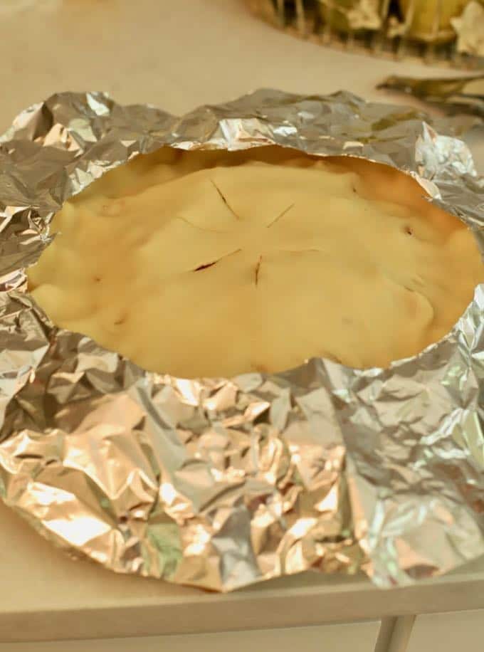 A pie with strips of aluminum foil covering the outside crusts to prevent over browning. 