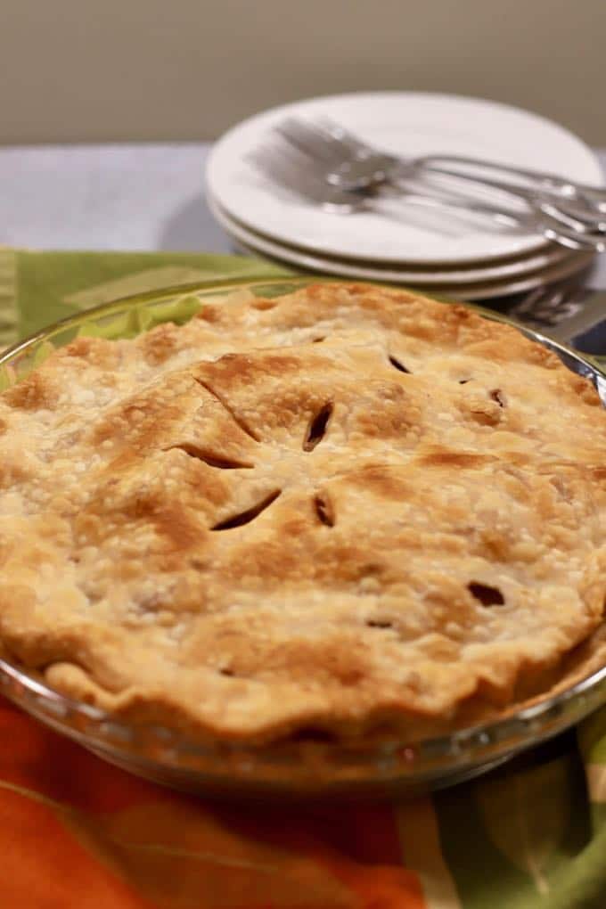 A pear pie out of the oven with a stack of white plates and forks in the background.