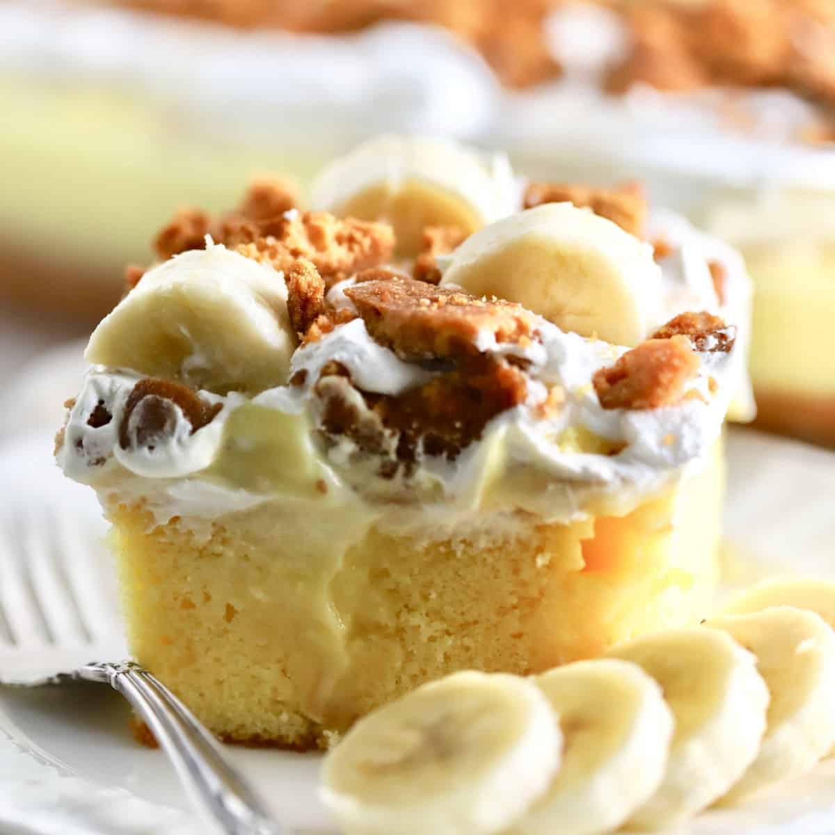 A piece of Southern Banana Pudding Poke Cake on a white plate with a fork.