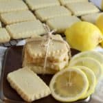 A stack of lemon shortbread cookies tied with a piece of string and lemon slices on a plate.