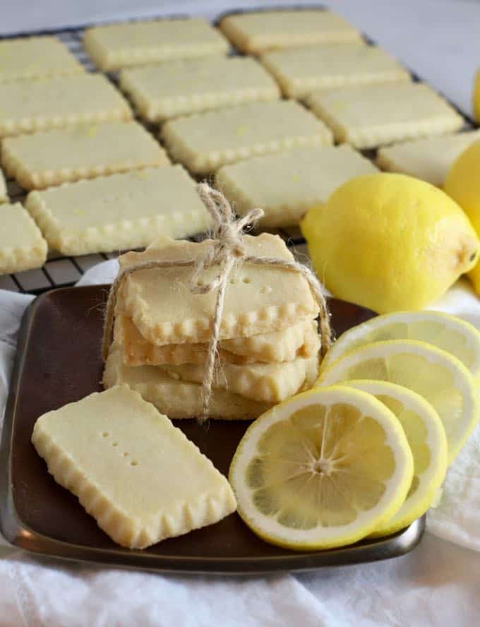 A stack of lemon shortbread cookies tied with a piece of string and lemon slices on a plate.