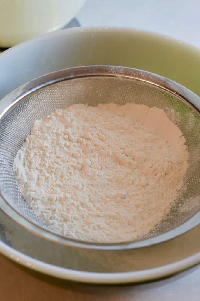 using a wire strainer to sift flour into shortbread cookie dough.