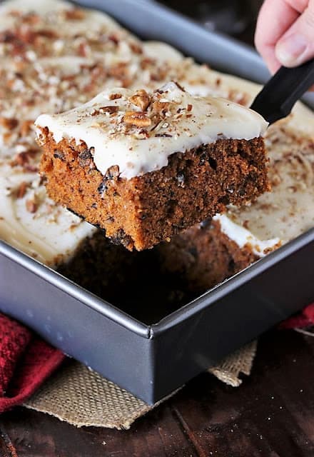 A slice of carrot Cake Sheet Cake being held above the pan.