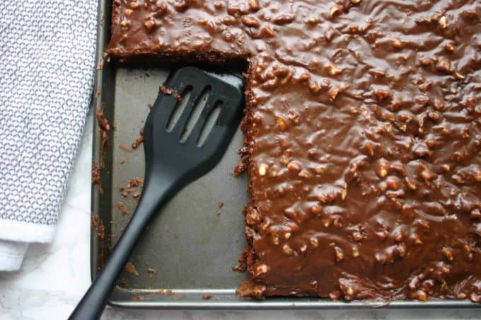 Cutting a piece of chocolate sheet cake with a pancake turner.