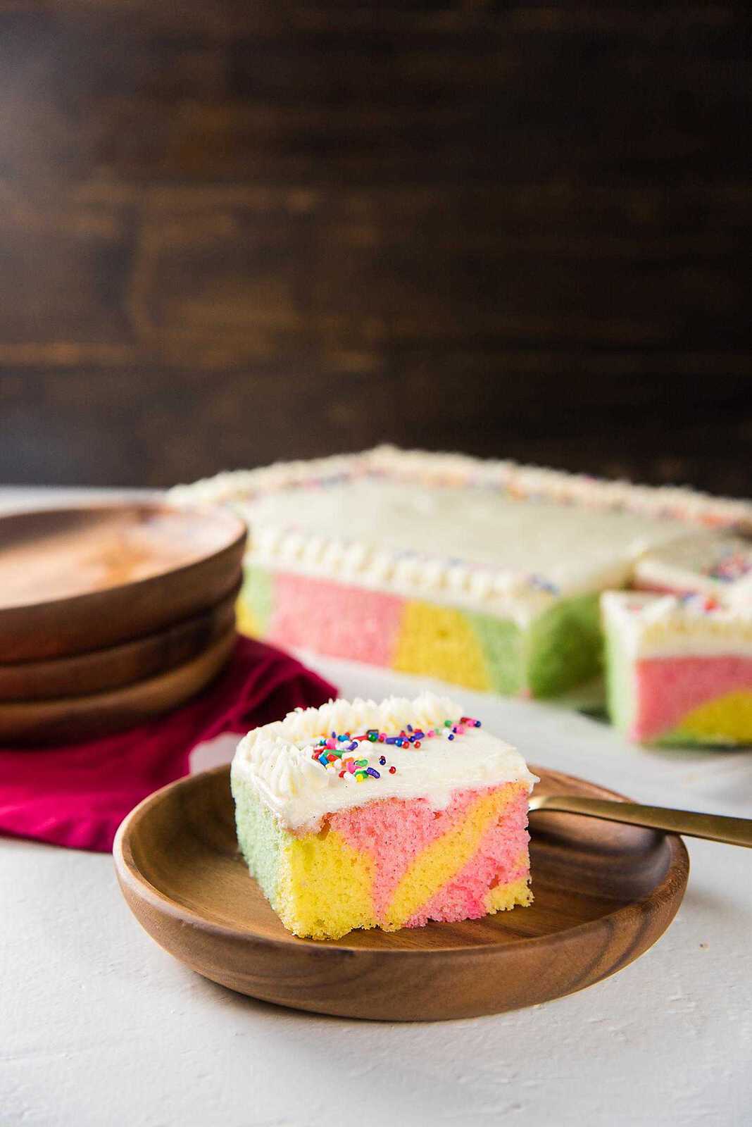 A slice of swirled pastel sheet cake with the whole cake in the background.