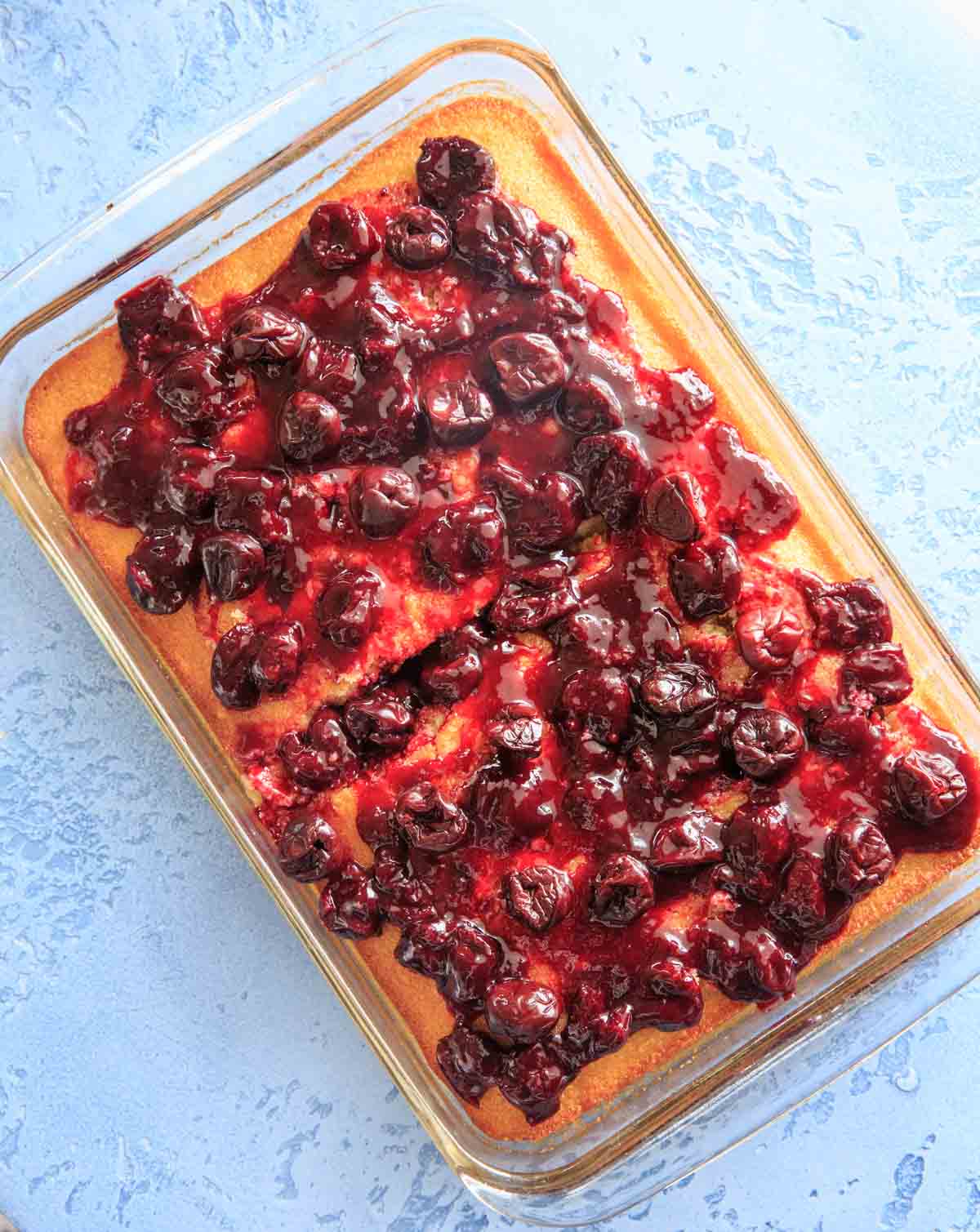 White sheet cake with cherry glaze topping in a glass dish.