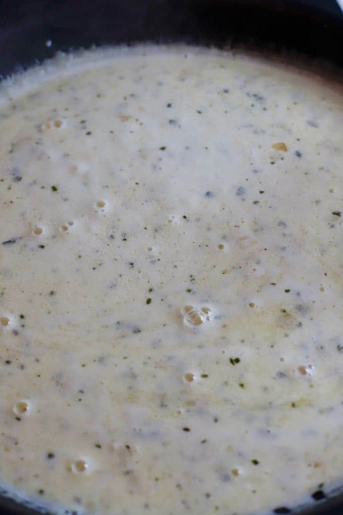 Heavy cream and parmesan cheese bubbling in a skillet. 