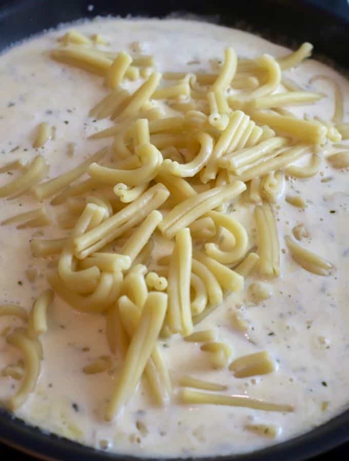 Pasta being added to a sauce of heavy cream and parmesan cheese in a skillet. 