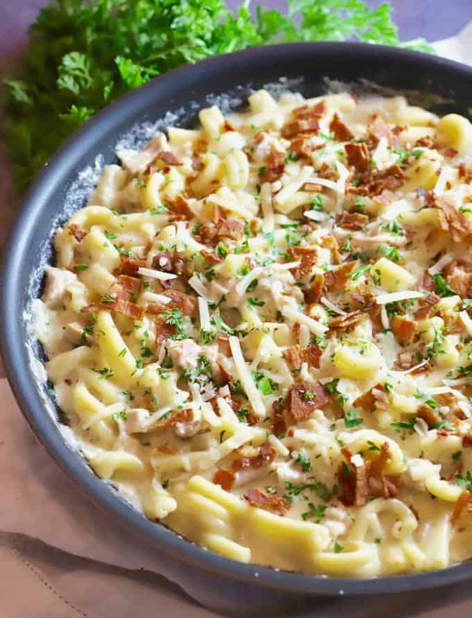 Chicken and bacon pasta in a skillet with a bunch of parsley in the background. 