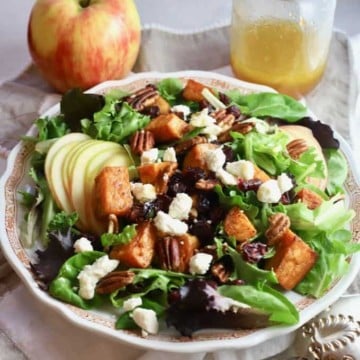 A large bowl with lettuce, sweet potatoes, apples, croutons and pecans for a Fall harvest salad.