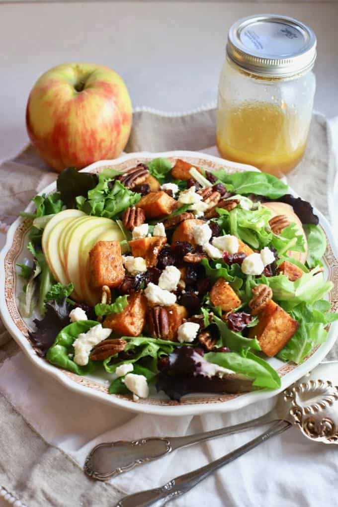 A large bowl with lettuce, sweet potatoes, apples, croutons and pecans for a Fall harvest salad. 