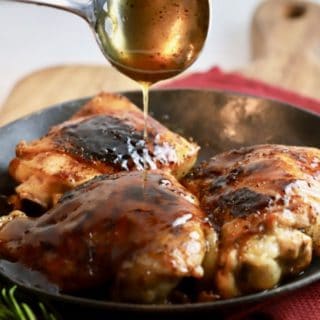 Three Honey Baked Chicken Thighs in a black skillet with glaze being spooned on.
