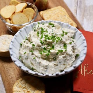 Blue Cheese Spread in a white bowl on a wooden cutting board with assorted crackers.