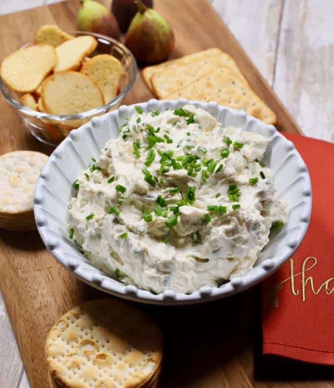 Blue Cheese Spread in a white bowl on a wooden cutting board with assorted crackers.