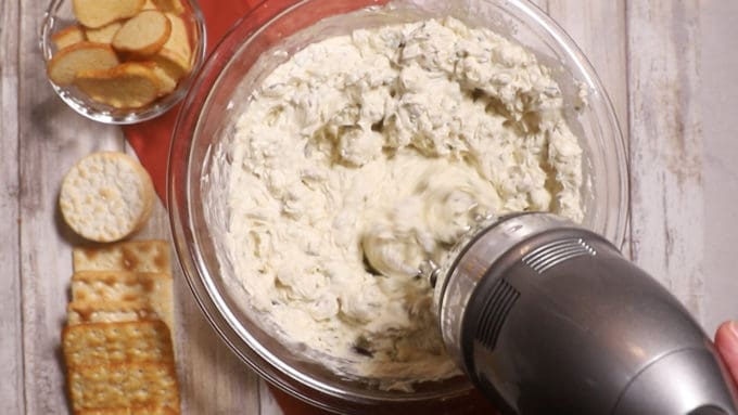 Mixing the ingredients for blue cheese dip in a clear glass bowl with an electric mixer. 