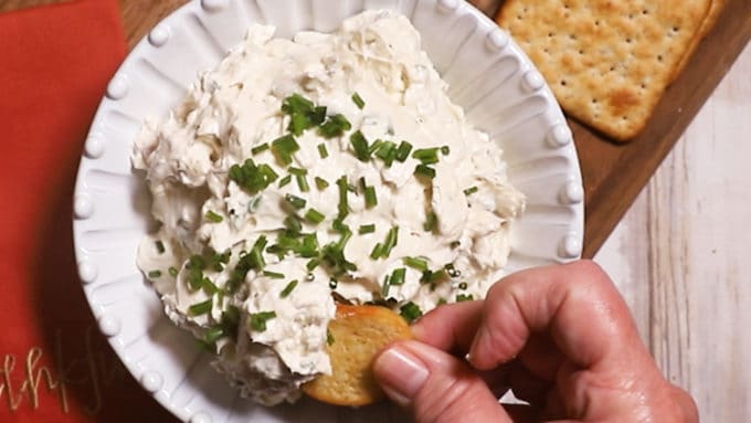 A cracker being dipped into blue cheese dip in a white bowl. 