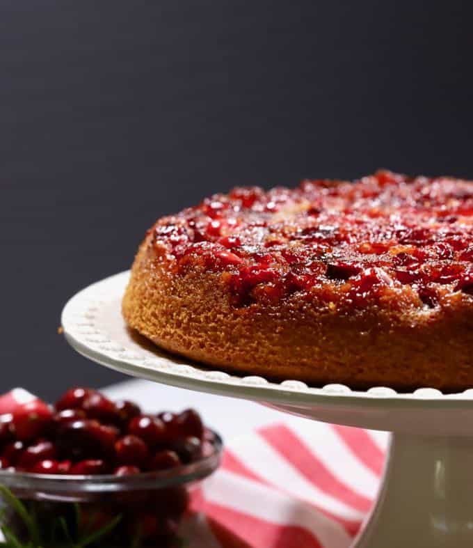 Cranberry Upside Down Cake on a white cake platter with a red and white napkin in the background.