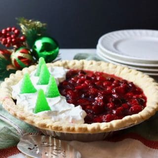 A beautiful cranberry pie on a dessert table with white plates in the background.